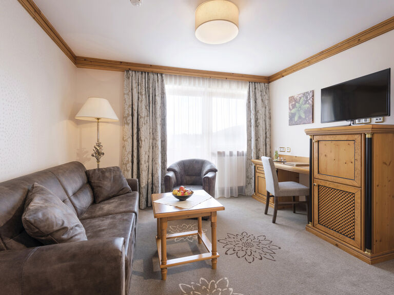 Stilvoll eingerichteter Wohnraum in einer Landhaussuite des Wellnesshotels Mooshof in Bodenmais mit bequemer Couch und moderner Flachbild-TV-Einheit.