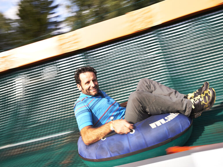 Ein lächelnder Mann fährt mit seinem Reifen eine Rutsche nach unten.