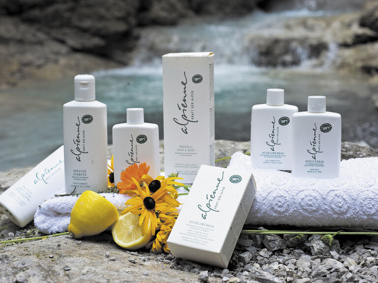 Hochwertige Pflegeprodukte der Marke Alpienne ruhen auf einem Felsen im Rahmen einer alpinen Umgebung mit Wasserfall.