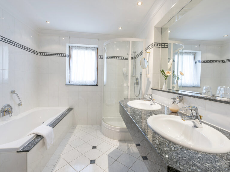 Das Badezimmer der Juniorsuite Classic im Wellnesshotel Mooshof im Bayerischen Wald präsentiert ein elegantes Design mit Waschbecken, Badewanne und Spiegel.