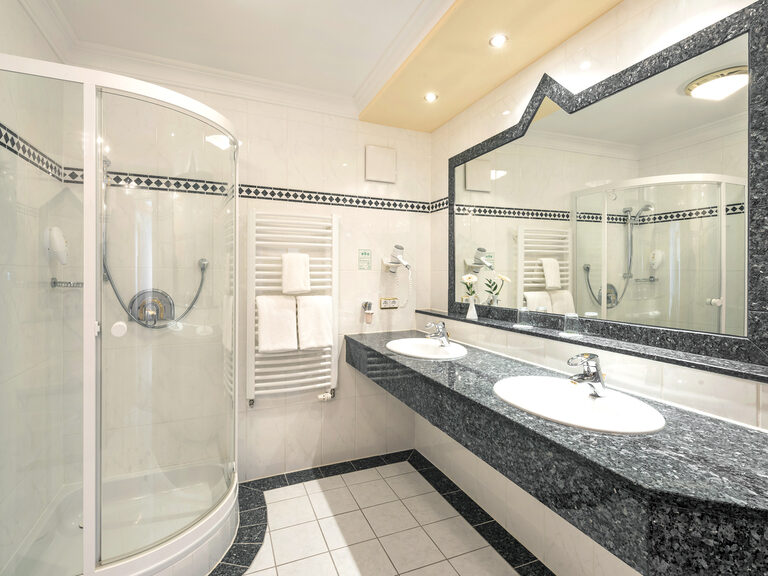 Luxuriöse Duschkabine neben einem beleuchteten Spiegel mit Waschbecken in der Komfortsuite des Wellnesshotels Mooshof in Bodenmais.