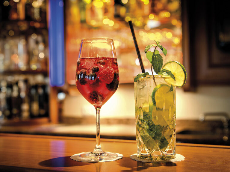 Zwei bunte Cocktails stehen auf dem stilvollen beleuchteten Bartresen des Wellnesshotels Mooshof im bayerischen Wald.