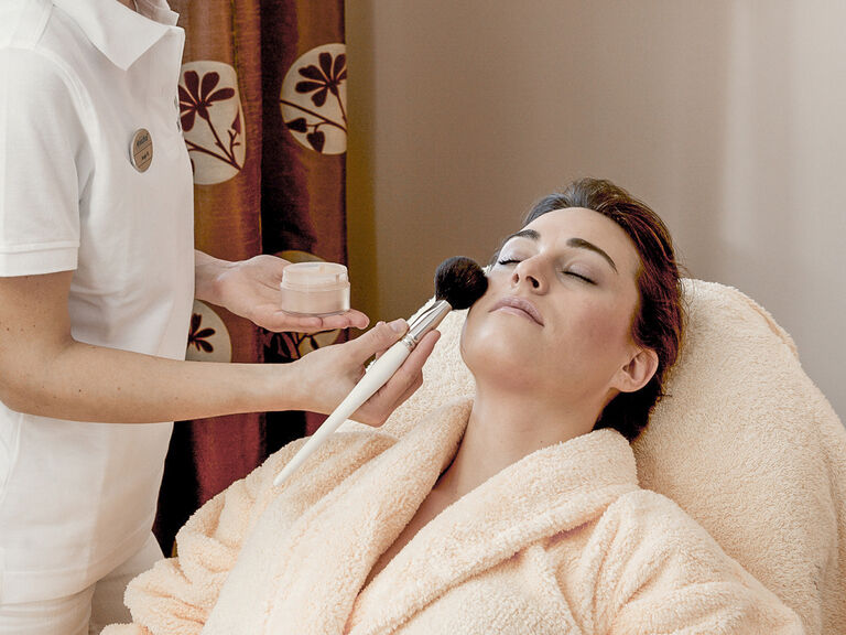 Eine Frau genießt eine Verwöhnbehandlung durch das Auftragen einer pflegenden Gesichtsmaske mit einem Pinsel im Vitalresort des Wellnesshotels Mooshof.