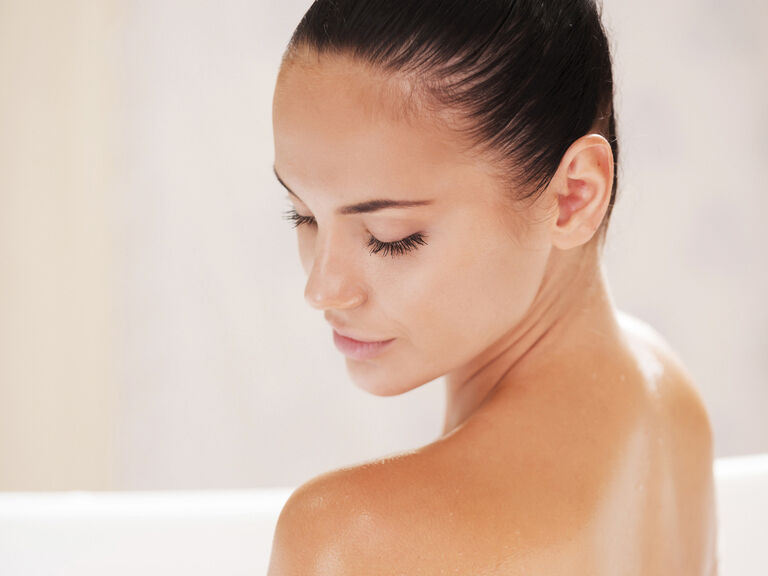 Eine Frau sitzt entspannt in einer Badewanne, umgeben von schaumigem Badeschaum.