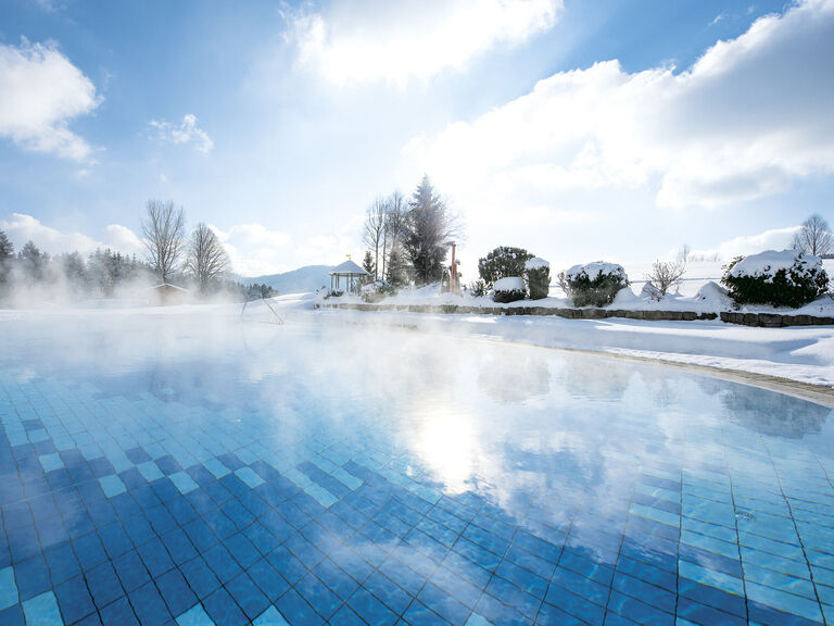 Der einladende beheizte Aussenpool im Wellnessbereich des Hotels Mooshof in Bodenmais unter einem blauen Himmel im Winter.
