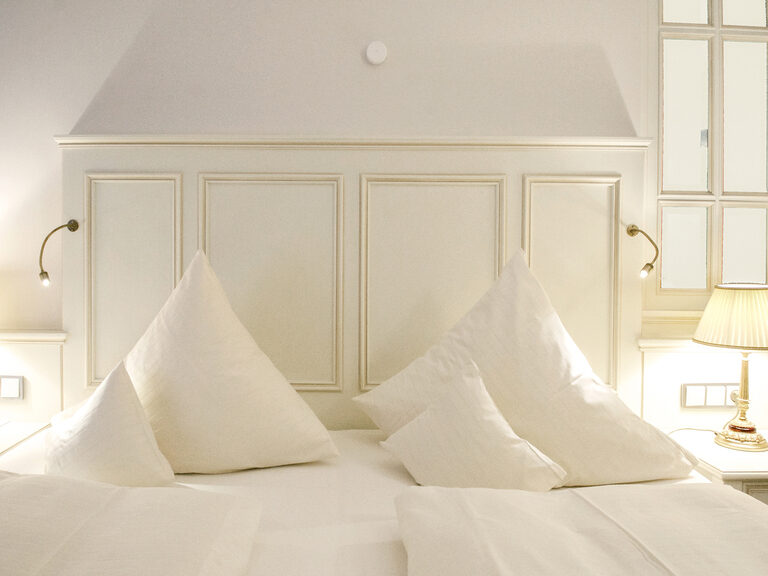 Elegant gestaltetes Bett mit weißen komfortablen Laken in der Berkhain Suite Deluxe des Wellnesshotels Mooshof in Bayern.