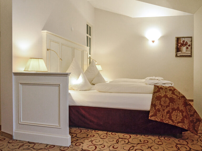Das Bett im Berkhain Suite Deluxe Zimmer des Wellnesshotels Mooshof in Bodenmais mit luxoriösem Bettgestell und Lampen mit sanftem Licht.
