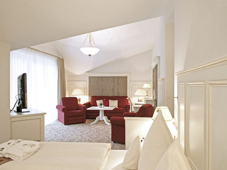 Das gemütliche Bett im Zentrum der Berkhain Suite Deluxe des Wellnesshotels Mooshof im Bayerischen Wald mit Blick auf den gemütlichen Wohnbereich mit Fernseher.