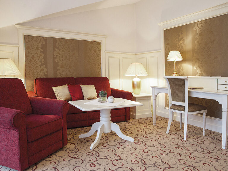 Stilvoll eingerichtetes Wohnzimmer in der Berkhain Suite Deluxe des Wellnesshotels Mooshof mit einem bequemen Sofa und einem eleganten Tisch zum Arbeiten.