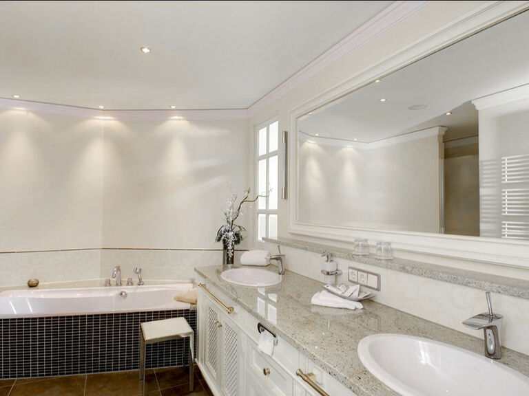 Modernes Badezimmerdesign der Birkenhain-Suite des Wellnesshotels Mooshof in Bodenmais mit zwei eleganten Waschbecken und einer Badewanne.