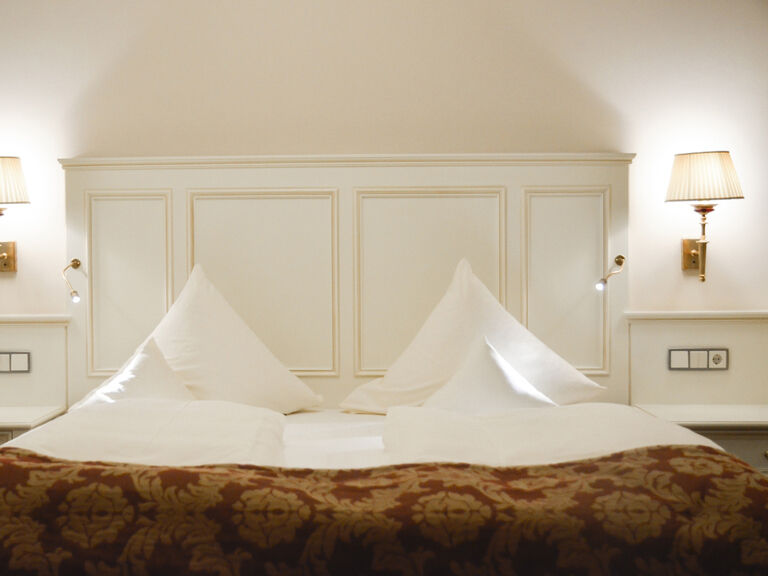 Einladendes Schlafzimmer mit einem großzügigen Bett und beiderseitiger Lampenbeleuchtung in der Birkenhain-Suite des Wellnesshotels Mooshof in Bodenmais.