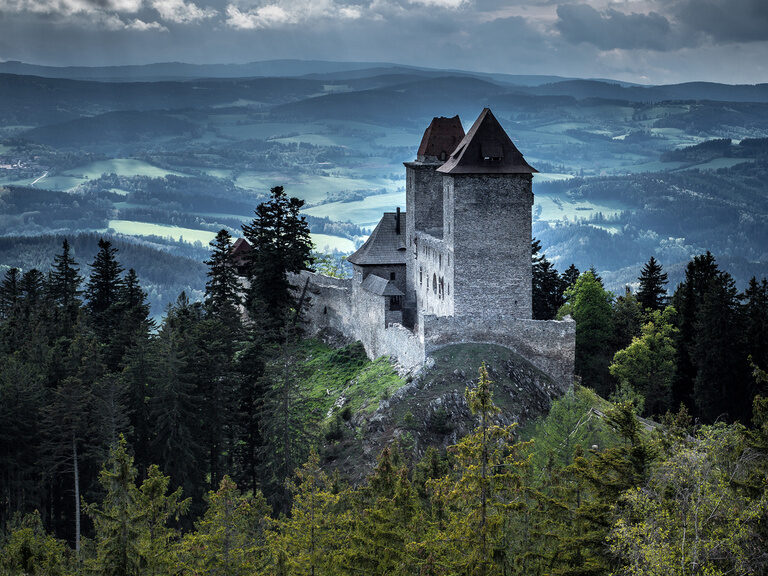Eine Burg auf einer Anhöhe in der morgendlichen Nebellandschaft.