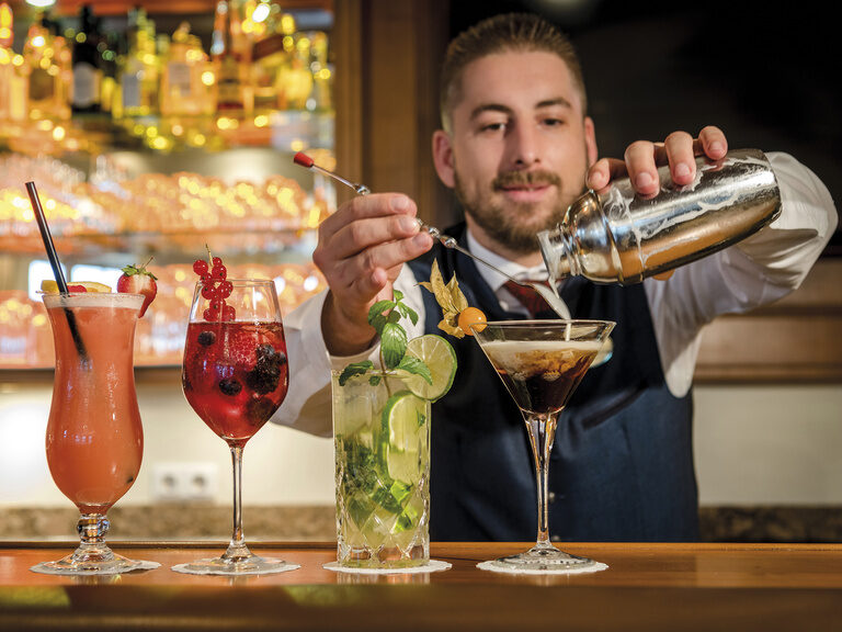 Ein Cocktail wird von einem Barkeeper im stilvollen Barambiente im Hotel Mooshof in Bodenmais vorbereitet.
