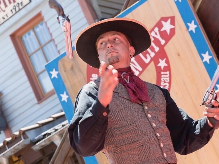 In Pullman City steht ein Mann mit Cowboyhut und Waffe vor einem Eingang in einen Laden.
