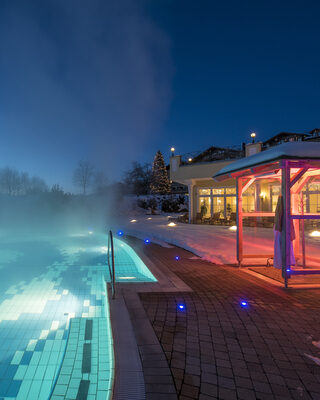 Der Aussenpool im Hotel Mooshof bei Nacht mit Lichtern.