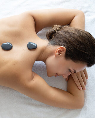 Die sanfte Steinmassage auf dem Rücken einer Frau bietet eine wohltuende Wellnesserfahrung im Wellnesshotel Mooshof im Bayerischen Wald.