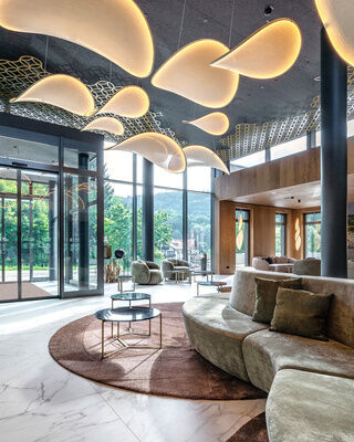 Eine gemütliche Lobby mit Naturmaterialien und großen Glasfenstern im Spa-Hotel Mooshof in Bodenmais.