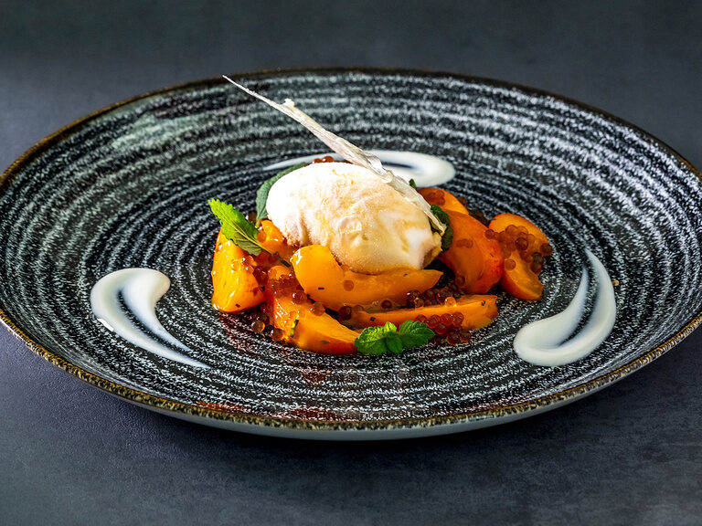 Eine köstliche kunstvoll verzierte Nachspeise serviert auf hochwertigem weißem Porzellan des Restaurants vom Wellnesshotel Mooshof im Bayerischen Wald.