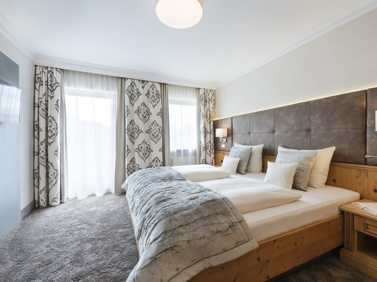Gemütliche Juniorsuite Classic im Wellnesshotel Mooshof im Bayerischen Wald mit modernen Möbeln und einem Flachbildfernseher vor einem komfortablen Doppelbett.