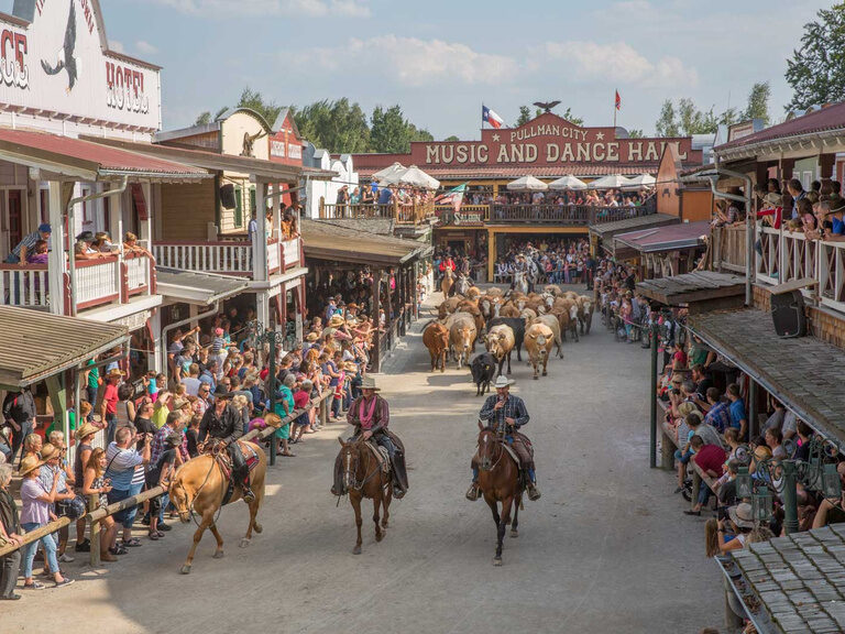 Drei Cowboys auf Pferden begeistern eine große Zuschauermenge in Pullman City.