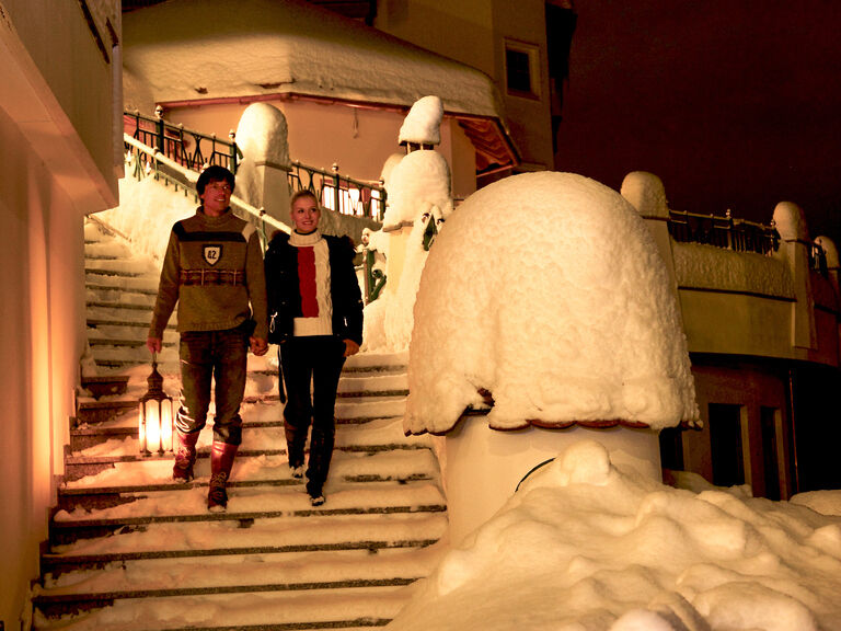 Ein paar steigt die Eingangstreppe des Mooshofs mit einer Laterne herunter um zu einer Wanderung bei Nacht aufzubrechen.