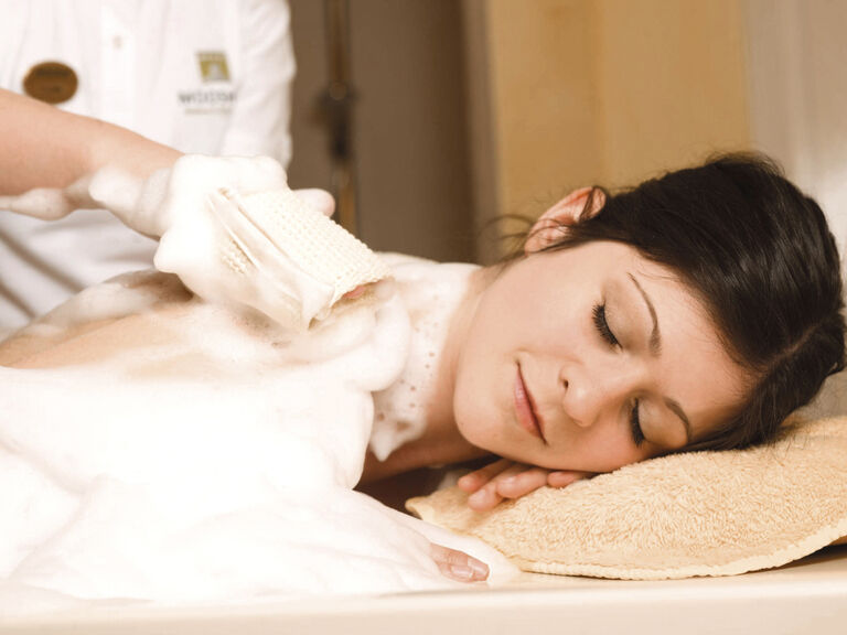 Eine Frau liegt auf einem Massagetisch im Wellness & SPA Resort Mooshof und genießt eine entspannte Auszeit bei einer Massage mit Schaum.