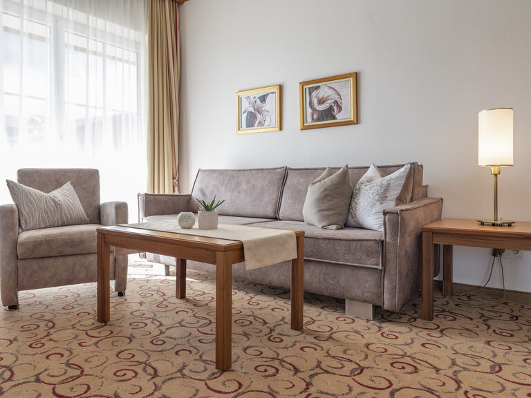 Zwei gemütliche Sofas mit Couchtisch im Wohnzimmer der Erkersuite Deluxe des Wellnesshotels Mooshof in Bayern neben dem Fenster mit Panoramaausblick.