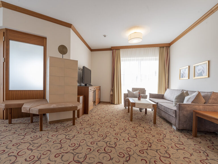 Stilvoll dekorierter Wohnraum der Erkersuite Deluxe im Wellnesshotel Mooshof mit Flachbild-TV und gemütlichem Sofa.