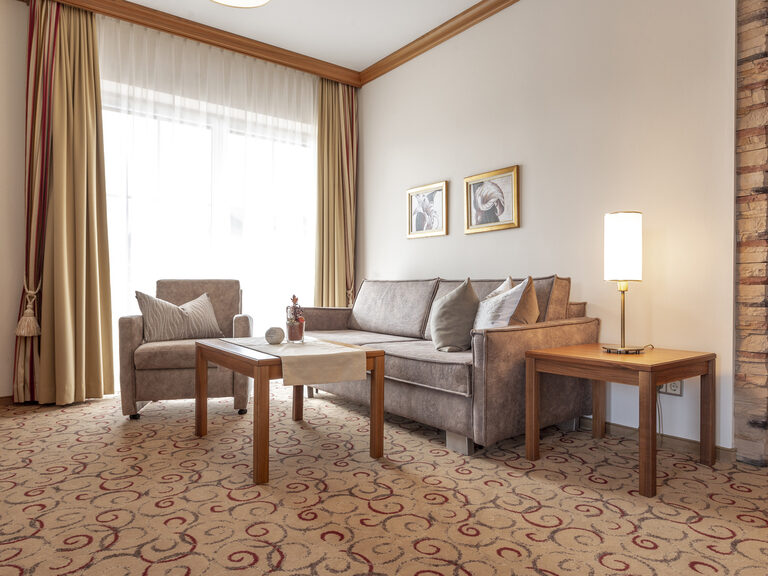 Ein Sofa und ein Sessel schaffen eine gemütliche Sitzgelegenheit im Wohnbereich der Erkersuite Deluxe des Hotels Mooshof in Bodenmais.