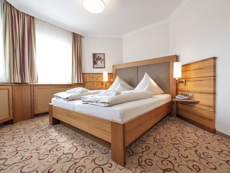 Das bequeme Doppelbett in der Erkersuite des Wellnesshotels Mooshof im Bayerischen Wald mit eleganten Nachttischen.