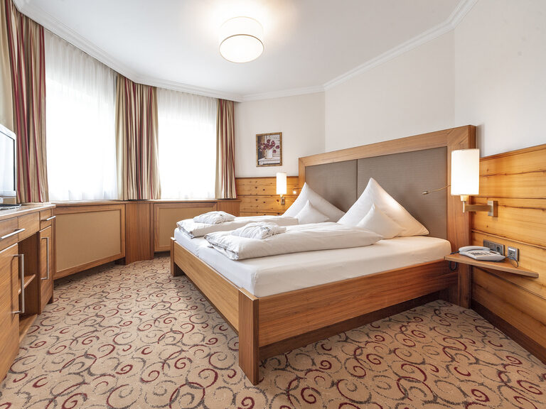 Der gemütliche Schlafbereich mit einem komfortablen Doppelbett und Fernseher in der Erkersuite des Wellnesshotels Mooshof in Bodenmais.