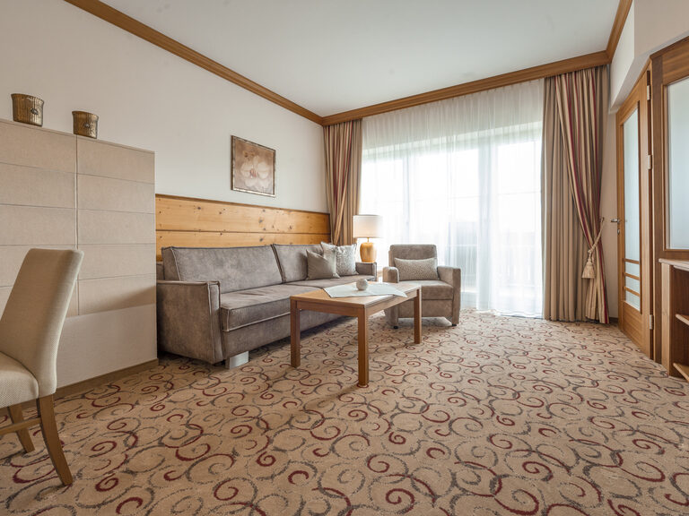 Das wohnliche Zimmer in der Erkersuite des Wellnesshotels Mooshof im Bayerischen Wald mit gemütlicher Couch und modernen Fernseher.