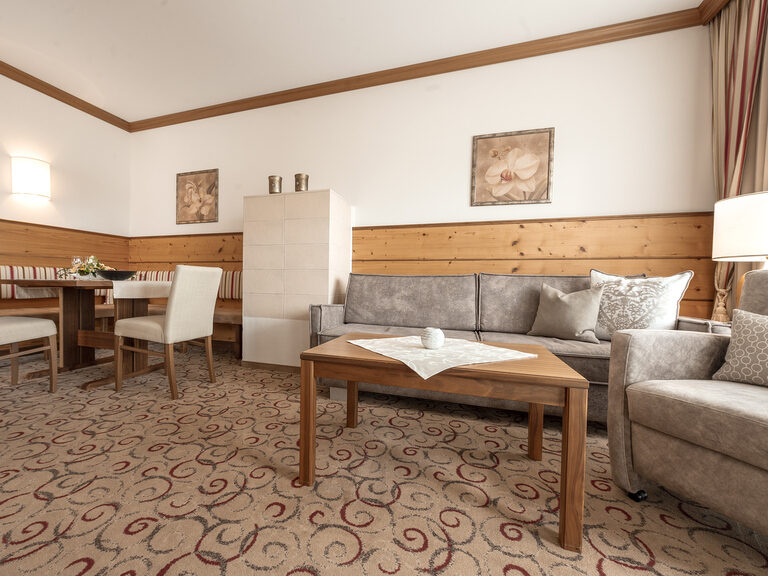 Das Wohnzimmer in der Erkersuite des Wellnesshotels Mooshof in Bodenmais überzeugt mit zwei einladenden Sitzmöglichkeiten am hellen Fenster und einem Tisch.