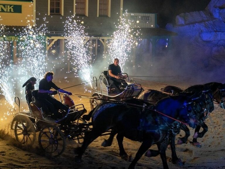 Eine Gruppe von Menschen fährt nachts während einer Feuershow auf einer Pferdekutsche durch Pullman City.