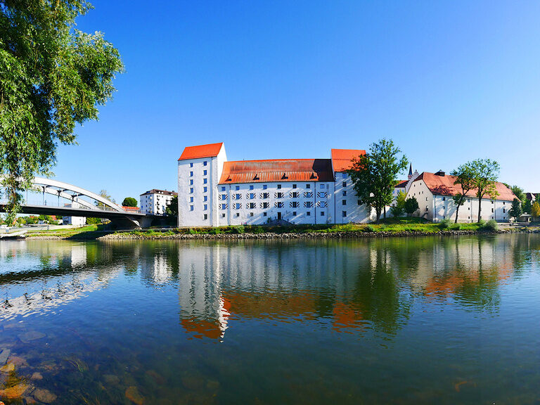 Eine ruhige Wasserfläche mit der Stadtsilhouette von Straubing im Hintergrund bei Nacht.