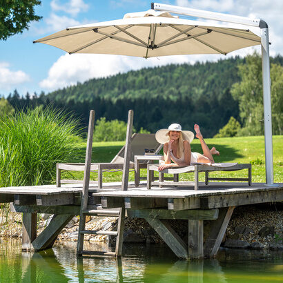 Die Urlauberin genie&szlig;t die Ruhe auf dem Steg des Mooshof-Resorts unter einem schattenspendenden Schirm.