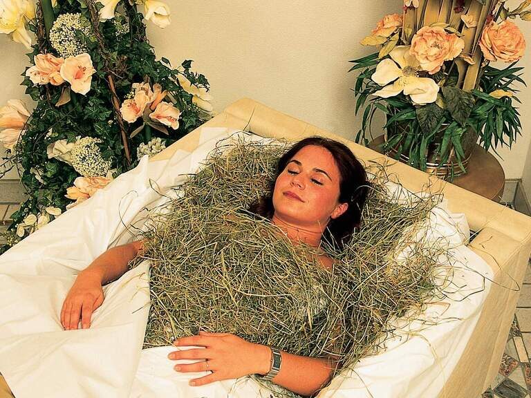 Eine Person ruht auf einem mit Heu bedeckten Bett in einem gemütlichen Ambiente des Wellnesshotels Mooshof im bayerischen Wald..