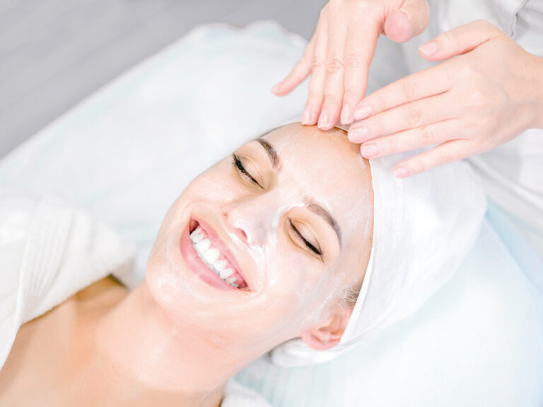 Eine Kosmetikerin trägt eine pflegende Maske auf das Gesicht eines Hotelgasts des Wellnesshotels Mooshof in Bayern auf.