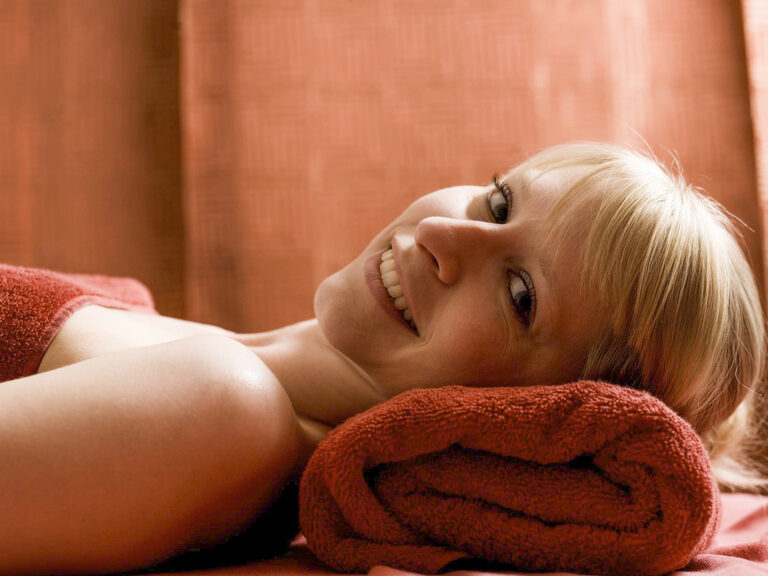 In dem Wellnessbereich des Hotels Mooshof in Bodenmais liegt eine Frau auf weichen, roten Handtüchern zur Erholung.