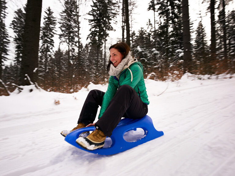 Eine Wintersportlerin genießt den Schnee beim Schlittenfahren im Bayerischen Wald.