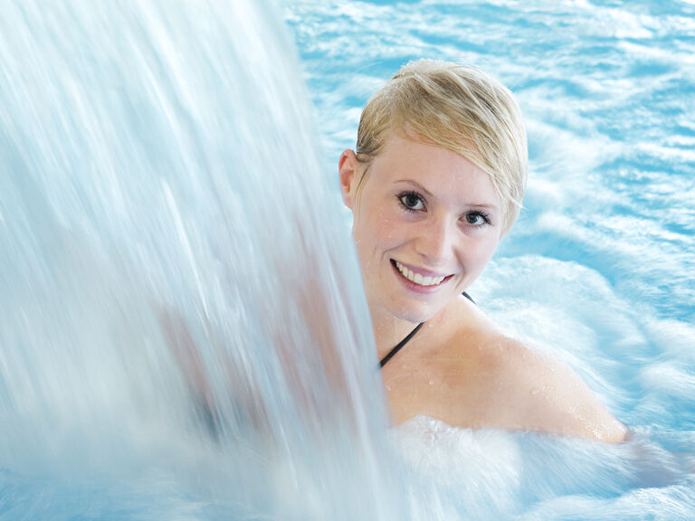 Im Innenpool sprudelt ein Wasserfall herunter unter dem sich eine Frau entspannt.