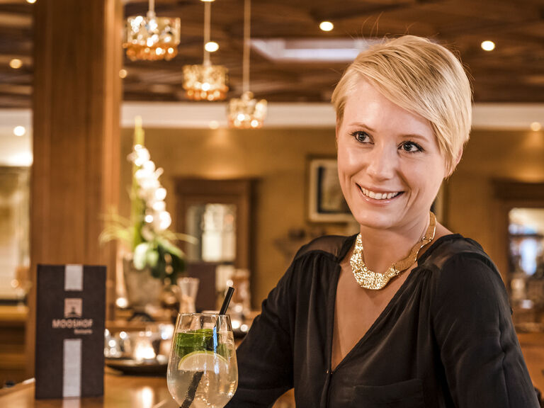 Ein Glas Wein steht vor einer lächelnden Frau an der Bar.