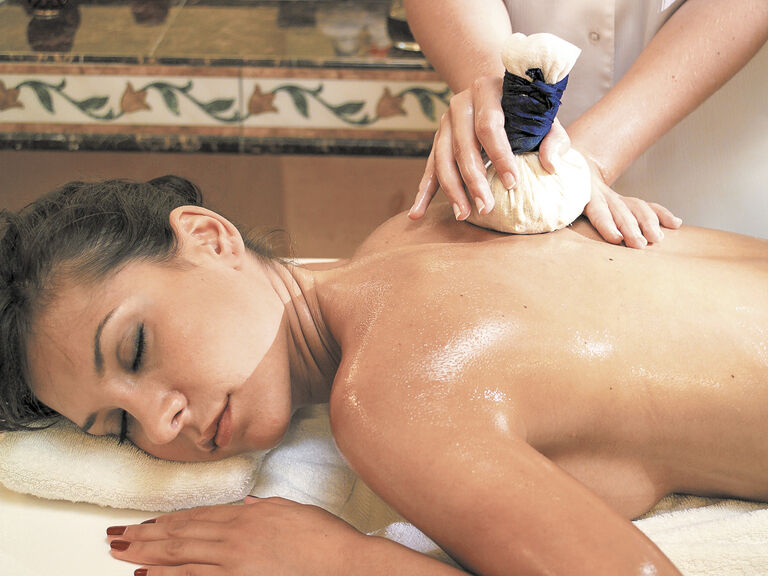 Eine Frau entspannt sich bei einer Massage mit Öl und einem Kräuterwickel im Spa des Hotels Mooshof in Bodenmais.