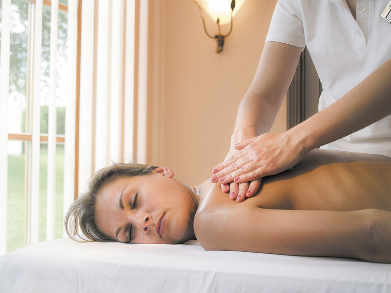 Eine Kosmetikerin verabreicht einer Frau eine wohltuende Rücken Massage im Wellnessbereich des Hotels Mooshof in Bodenmais.
