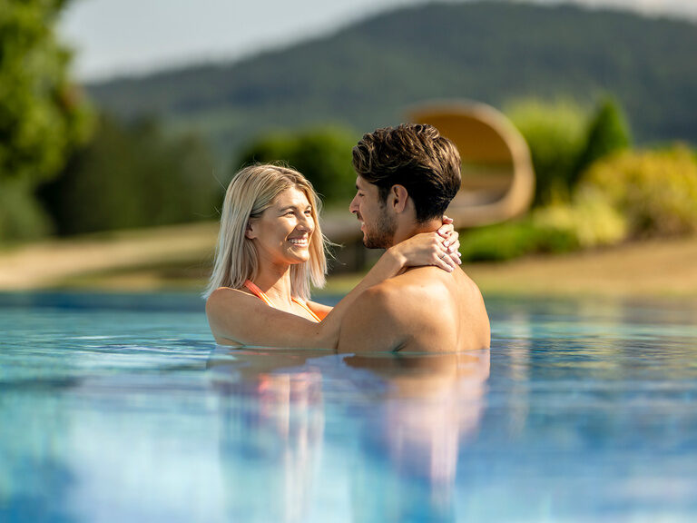 Ein Paar genießt romantische Zweisamkeit im großzügigen Aussenpool des Wellnesshotels Mooshof in Bodenmais.