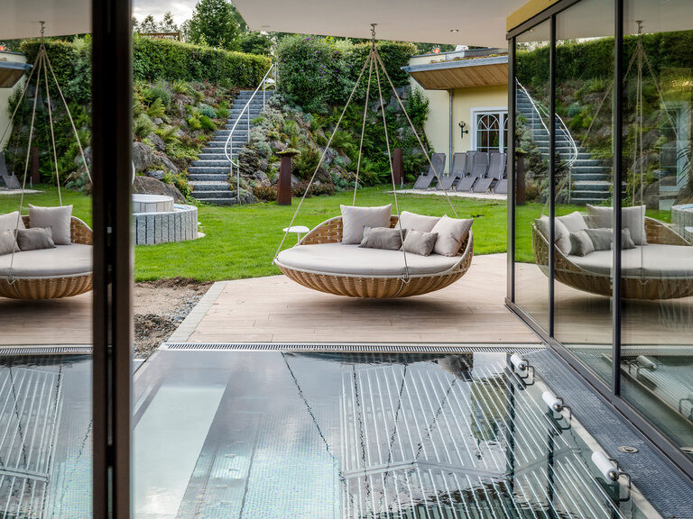Die bequeme Gartenschaukel lädt vor dem erfrischenden Aussenpool des Wellnesshotels Mooshof in Bodenmais zum Entspannen ein.