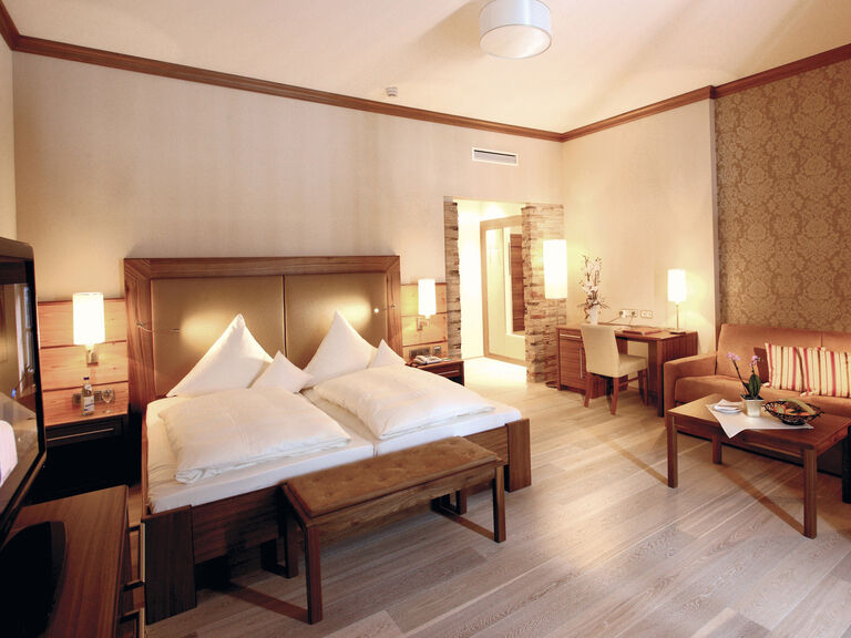 Helles Innenraumdesign der Gartensuite im Wellnesshotel Mooshof im Bayerischen Wald mit einem luxuriösen Bett und komfortabler Sitzgelegenheit zum Verweilen.