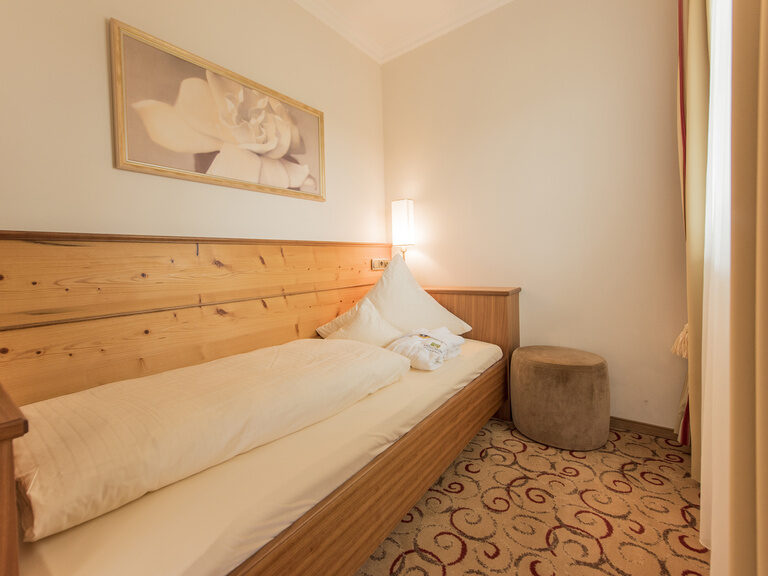 Das gemütliche Einzelbett steht in der Gartensuite Schwalbennest des Wellnesshotels Mooshof neben einem Fenster.