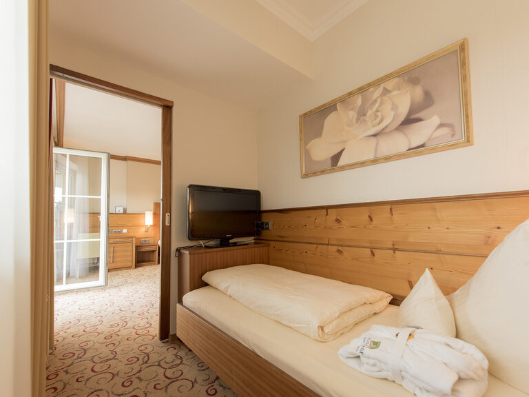 Einladende Schlafzimmergestaltung in der Gartensuite Schwalbennest des Wellnesshotels Mooshof im Bayerischen Wald, die ein bequemes Bett und eine moderne Unterhaltungsausstattung bietet.