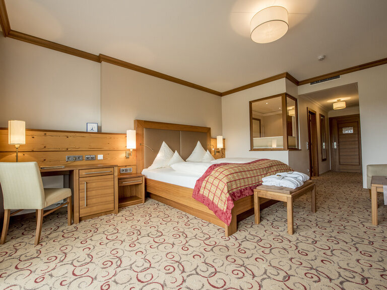 Stilvolle Einrichtung mit komfortablen Bett und praktischen Schreibtisch in der Gartensuite Schwalbennest des Wellnesshotels Mooshof in Bodenmais.